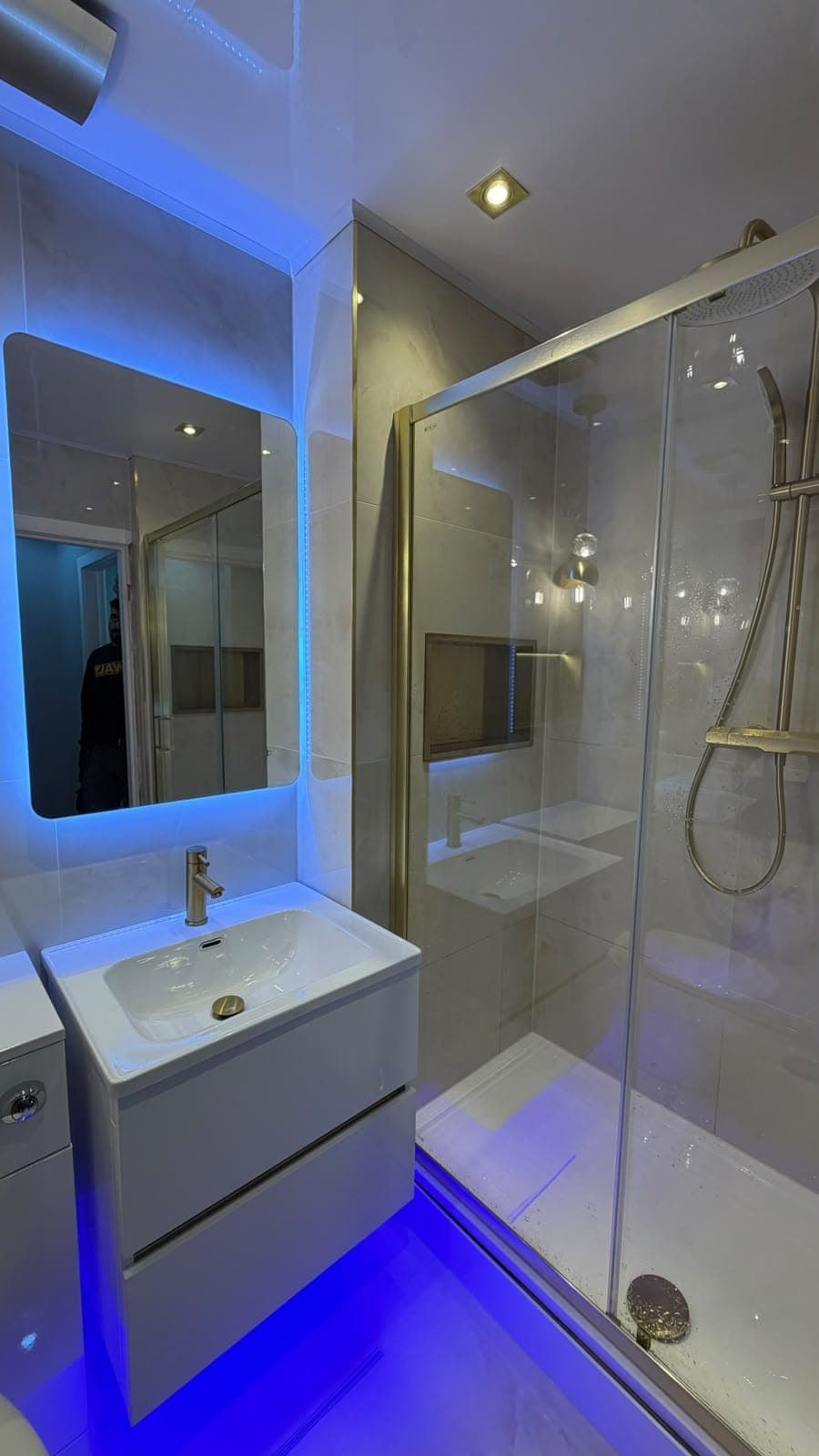 Bathroom with blue LED-lit mirror, glass walk-in shower and white floating vanity unit