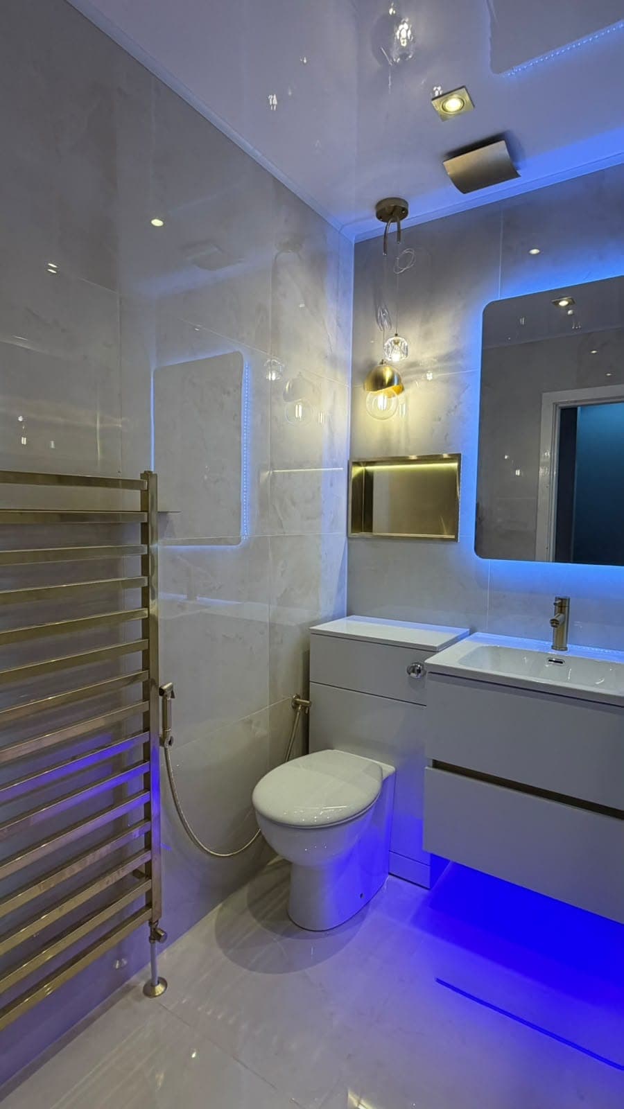 Compact bathroom with blue LED mirrors, brass heated towel rail and wall-hung vanity units