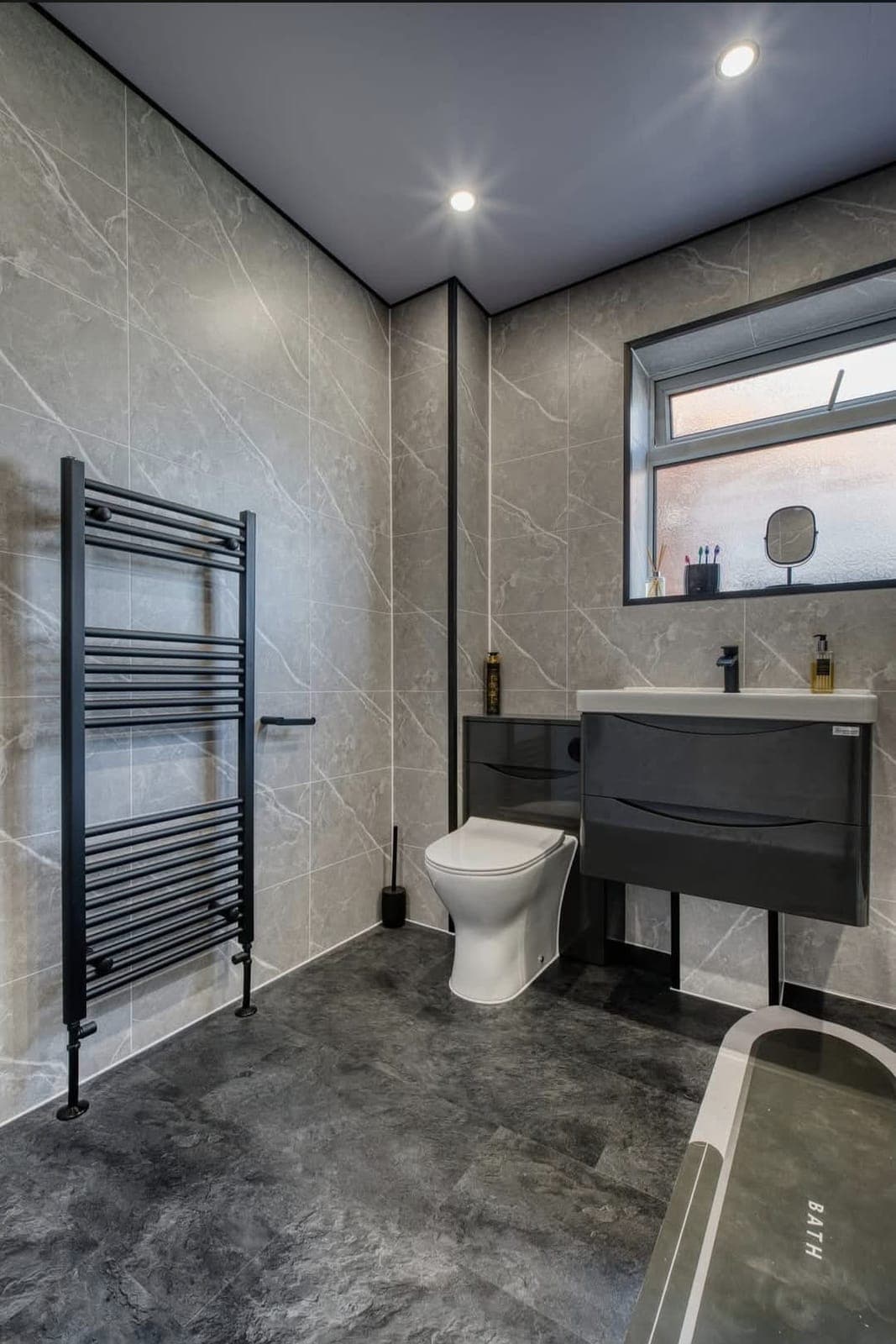 Bathroom with dark grey floating vanity, black towel radiator and freestanding bath beside the window