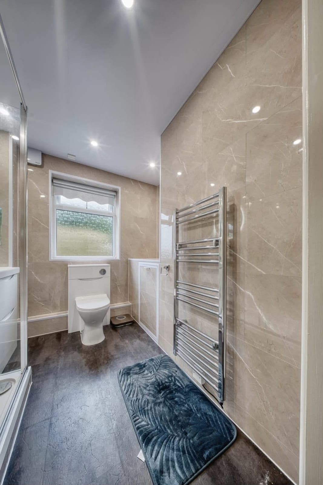 Bathroom with marble-effect wall tiles, glass shower enclosure and chrome towel radiator