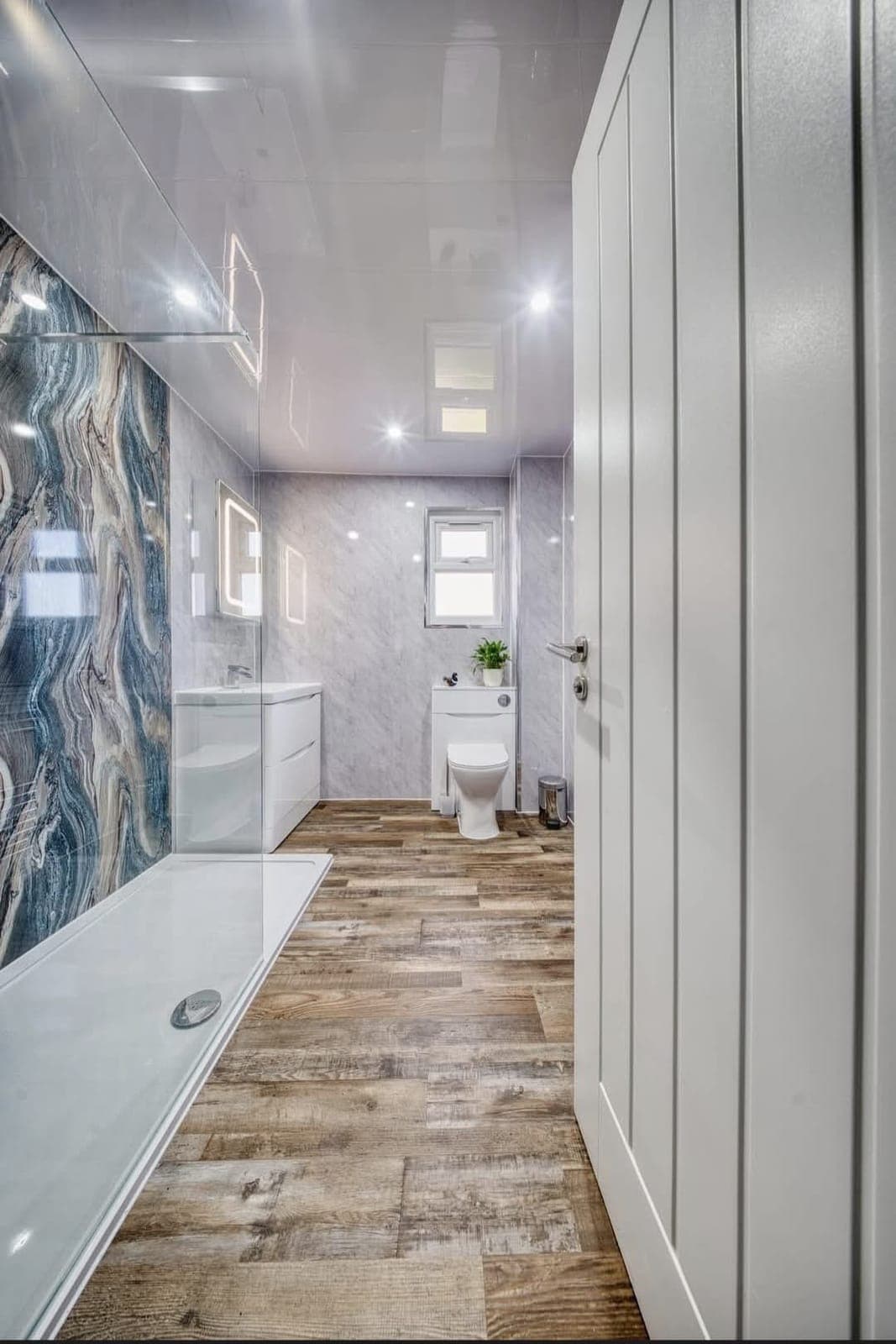 Long bathroom with blue marble feature wall, wood-effect flooring and fitted white wardrobes