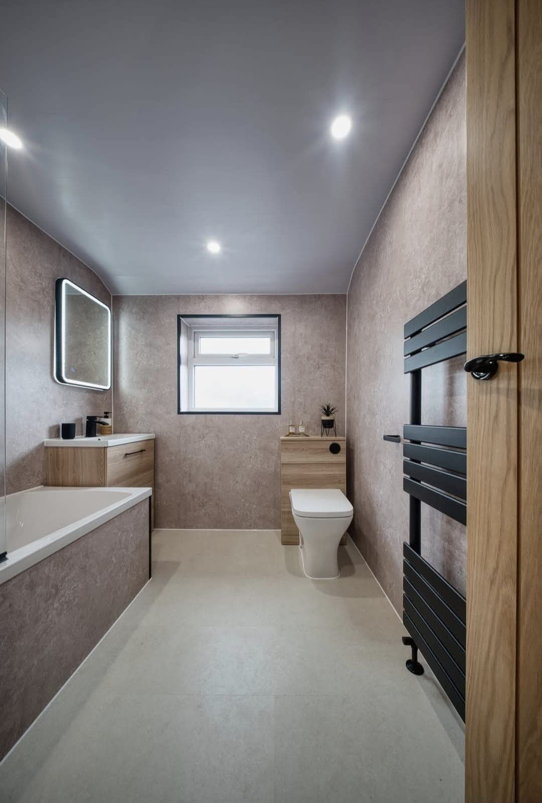 Bathroom with panelled bath, black towel radiator and warm beige wall panels