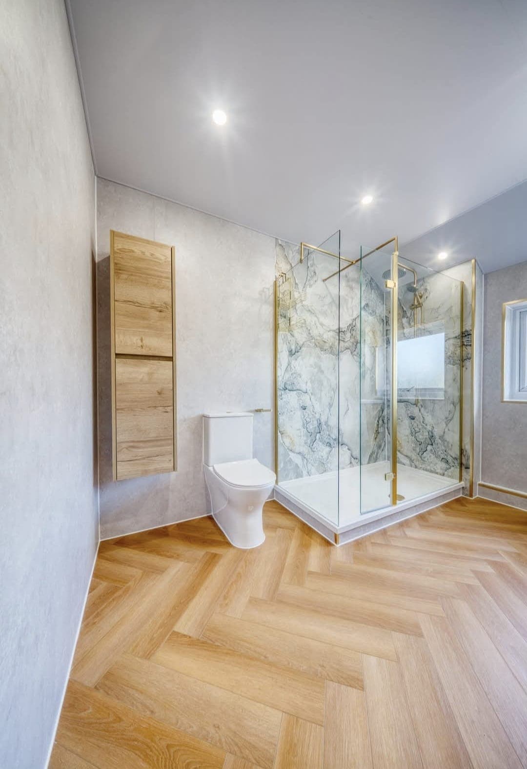 Compact bathroom with oak wall cabinets, glass shower and herringbone flooring