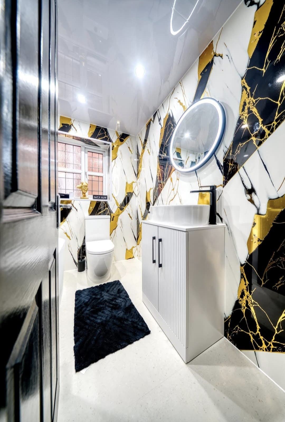 Toilet and vanity with round LED mirror against gold-veined marble wall panels