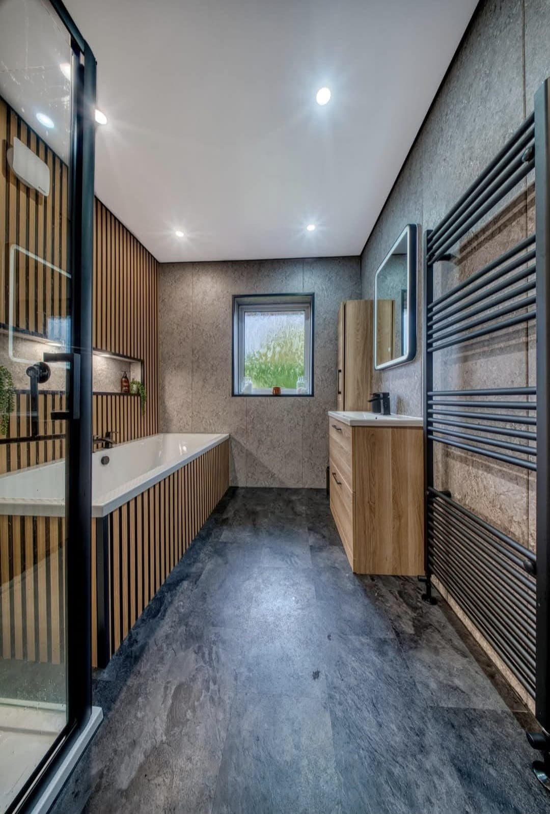 Bathroom with oak slatted panelling, black towel radiator and corner bath