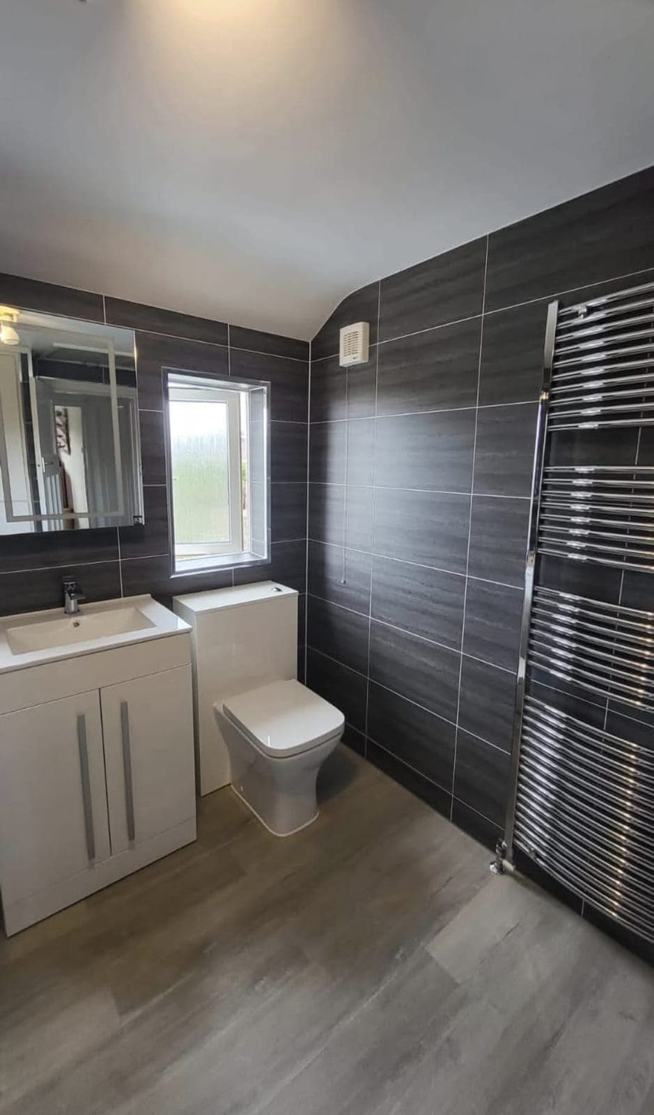 Bathroom with dark tiled wall, chrome heated towel rail and white vanity unit