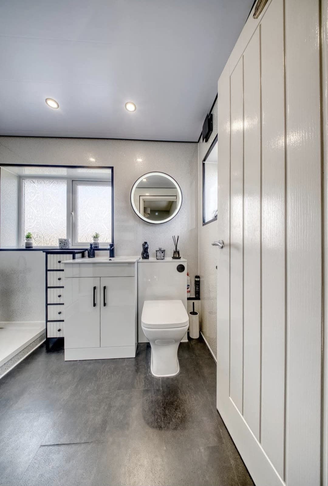 Bathroom with white vanity unit, round LED mirror and fitted wardrobes