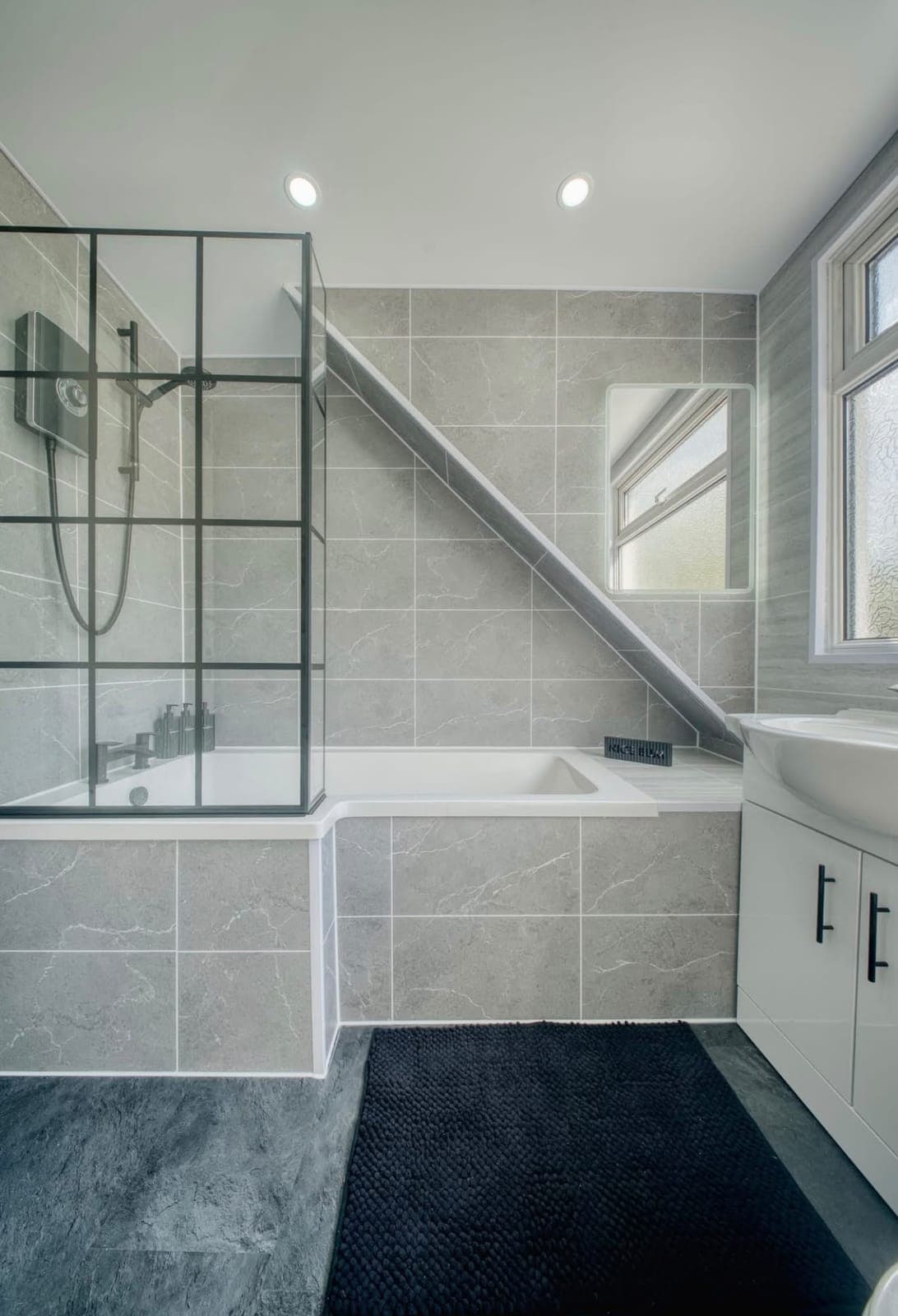 Loft-style bathroom with black-framed shower screen and tiled bath surround