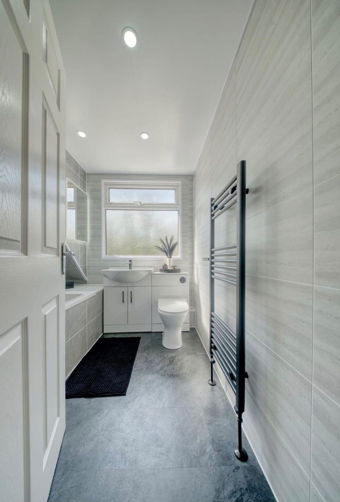 Long bathroom with black towel radiator, window and white vanity unit