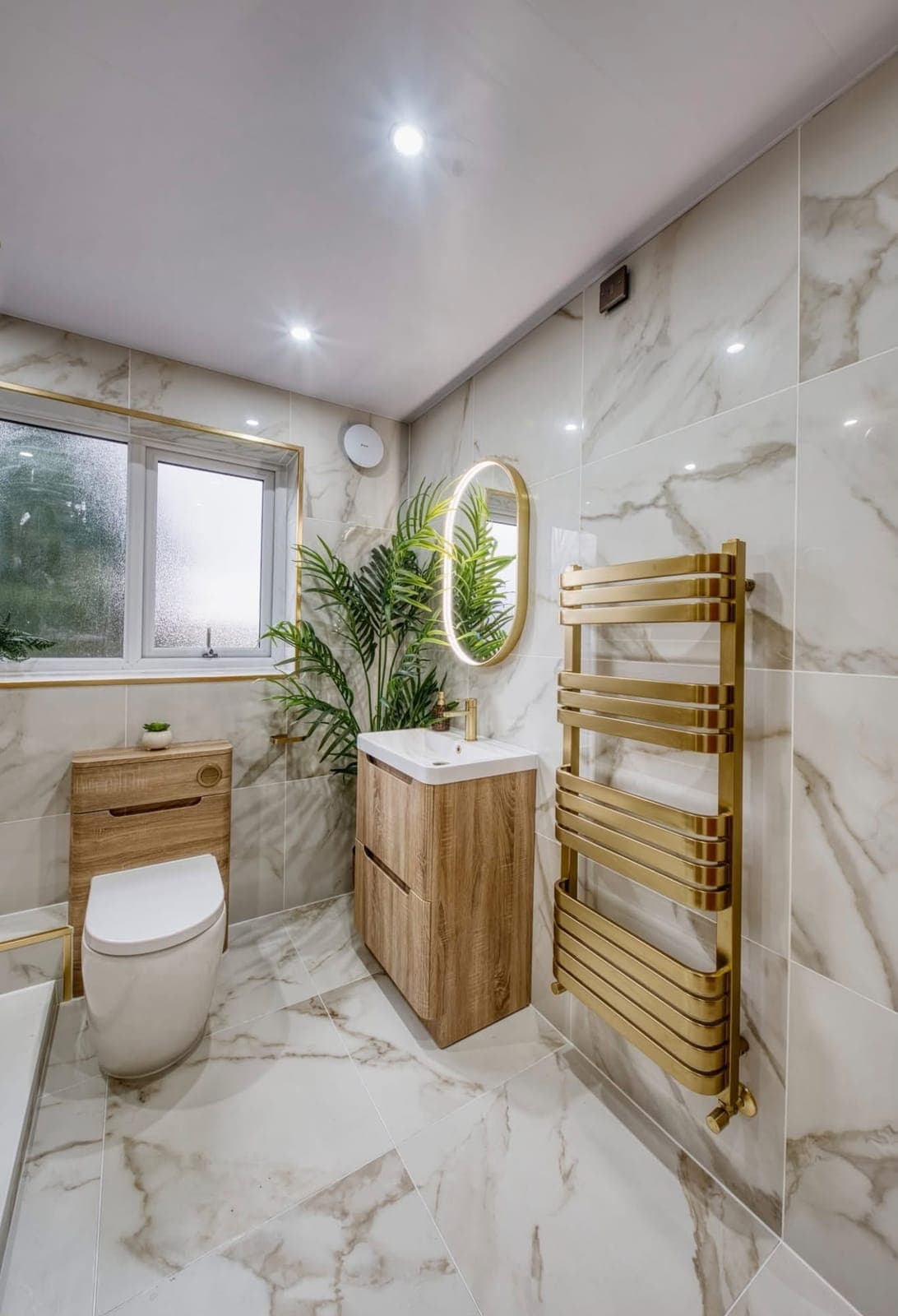 Marble-effect bathroom with gold heated towel rail, oak vanity and plants