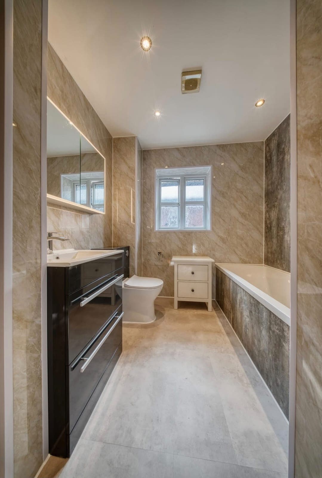 Bathroom with dark vanity unit, window and tiled bath surround