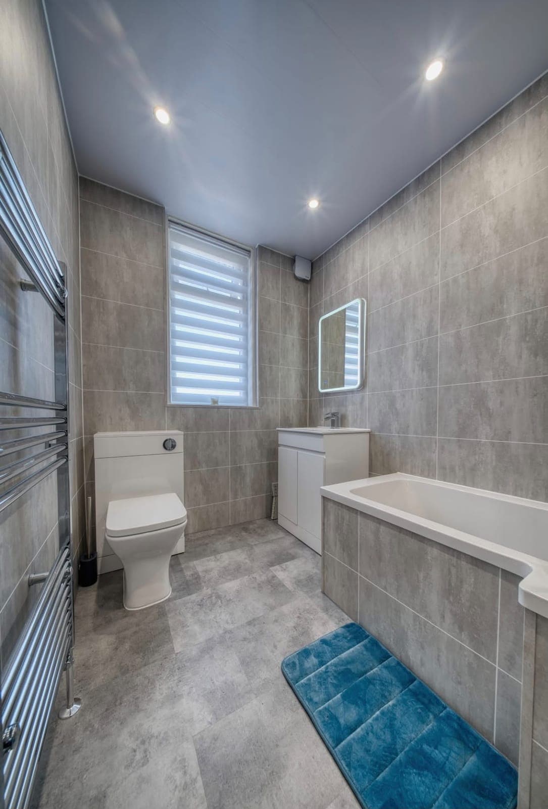 Bathroom with panelled bath, teal bath mat and chrome towel radiator