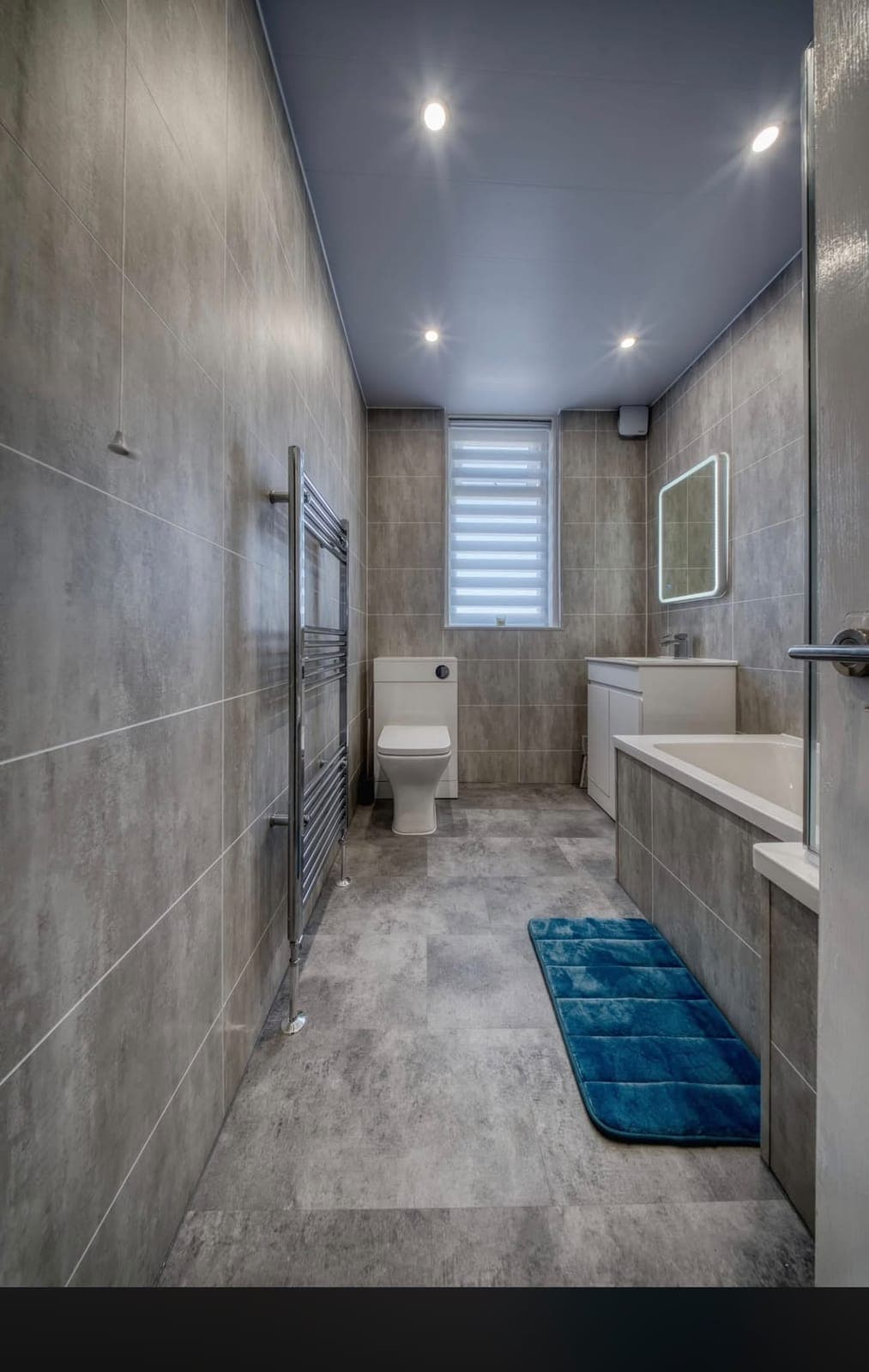 Long narrow bathroom with tiled walls, bath and chrome radiator