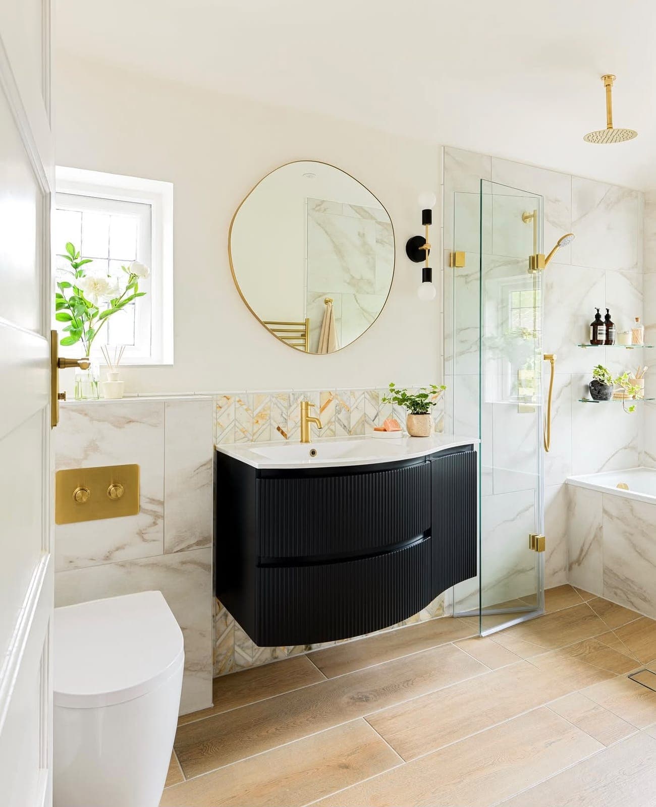 Marble bathroom with curved black vanity unit, oval mirror and brass fittings