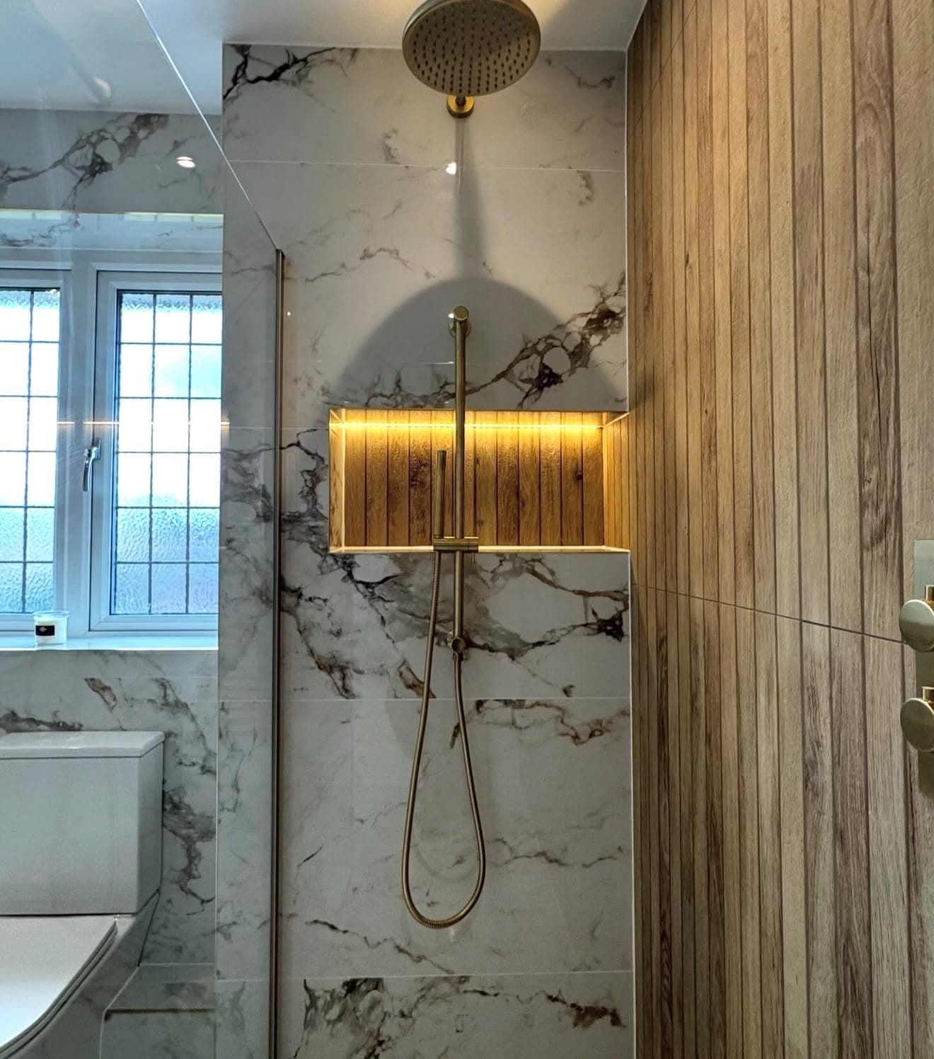 Marble shower wall with brass rain shower head and fluted timber panel