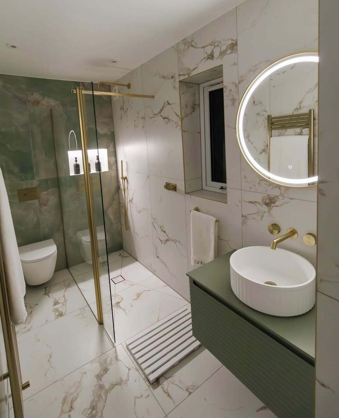 Walk-in shower with marble tiles, green vanity and round backlit mirror
