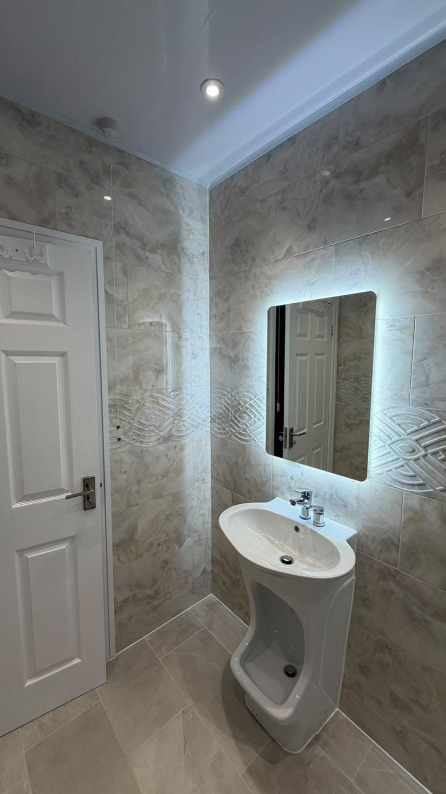 Compact cloakroom with backlit mirror, pedestal basin and marble-effect tiles