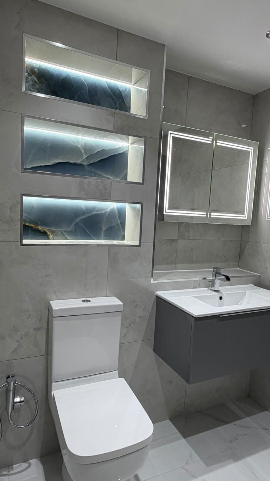 Bathroom with backlit shelving niches, mirror cabinet and dark floating vanity