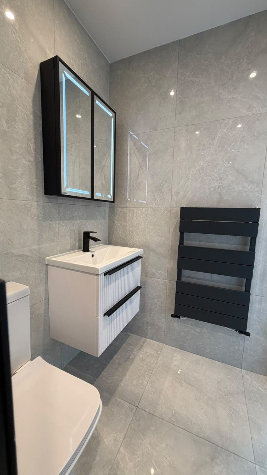 White vanity with black handles, mirror cabinet and black towel radiator