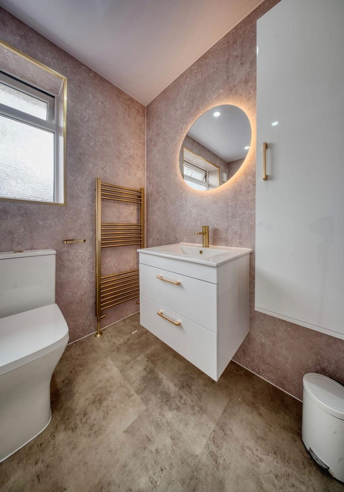 Bathroom with pink-toned walls, round backlit mirror and floating white vanity