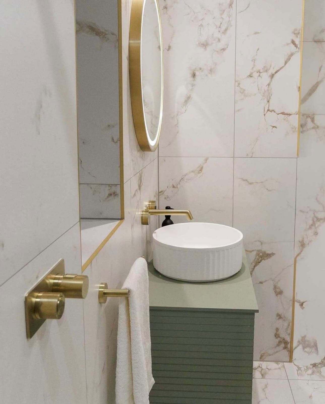 Round basin on a green wall-hung vanity with brass tap and marble wall tiles