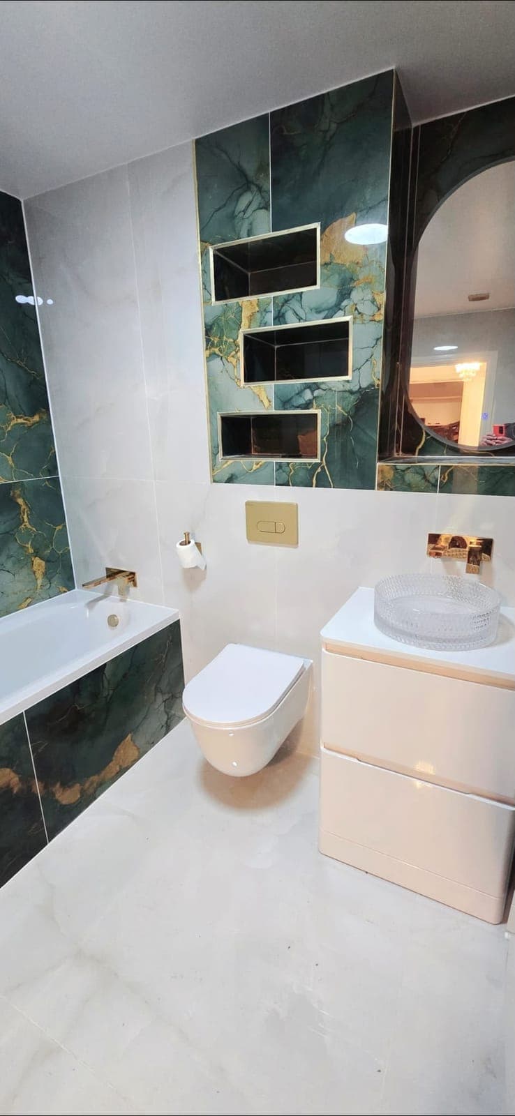 Green marble feature wall with recessed shelving, bath and wall-hung toilet