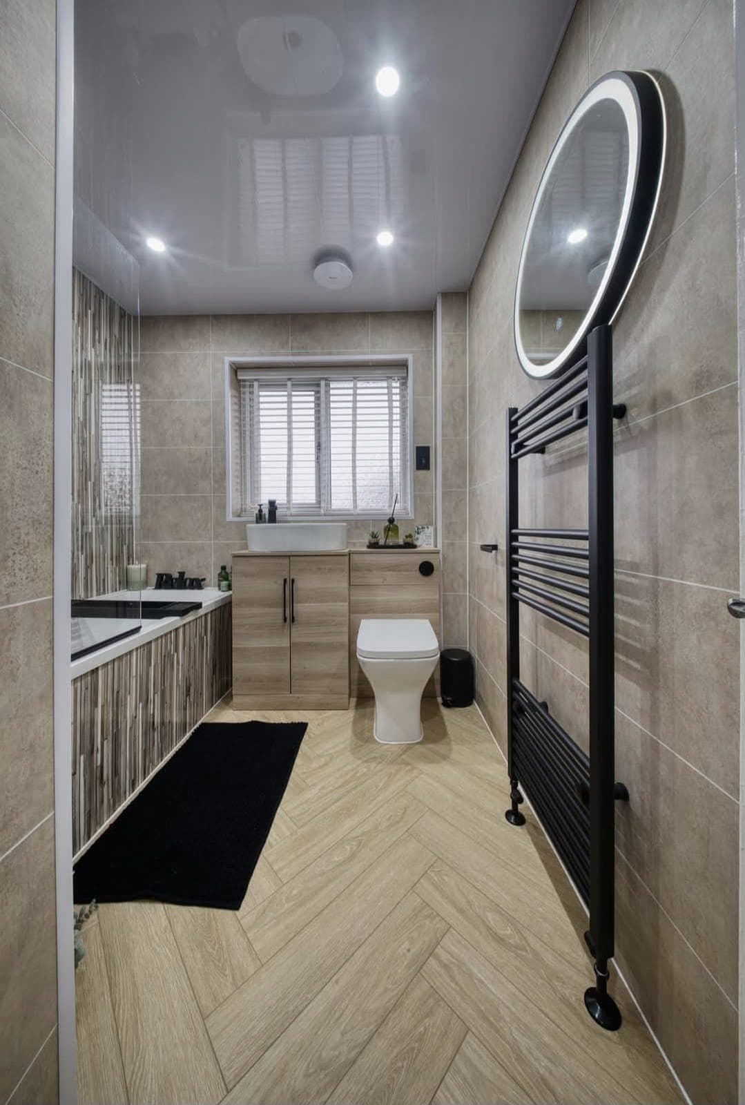 Herringbone-floor bathroom with panelled bath, round black-framed mirror and black towel radiator
