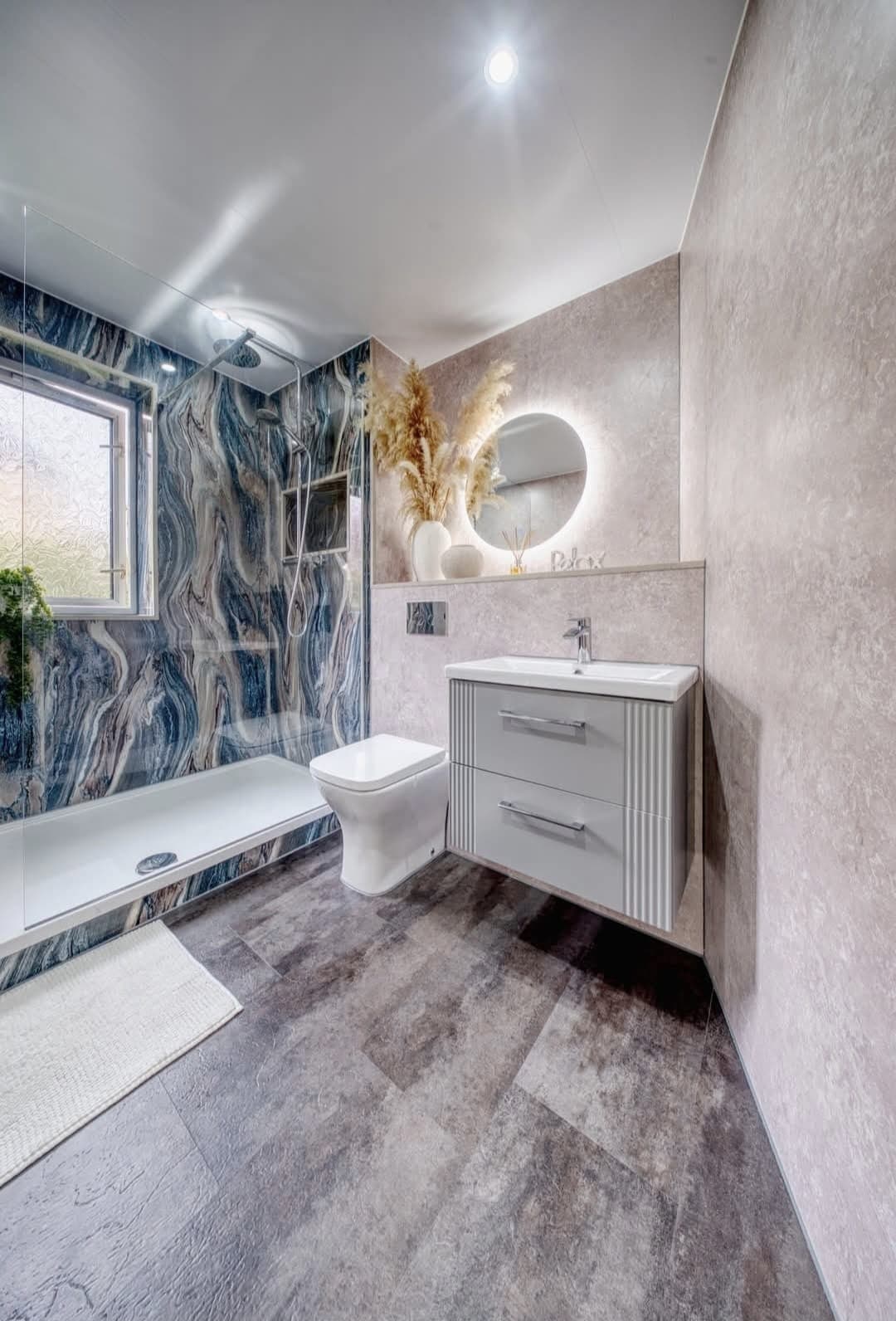 Bathroom with blue and grey marble shower wall, floating vanity and round mirror
