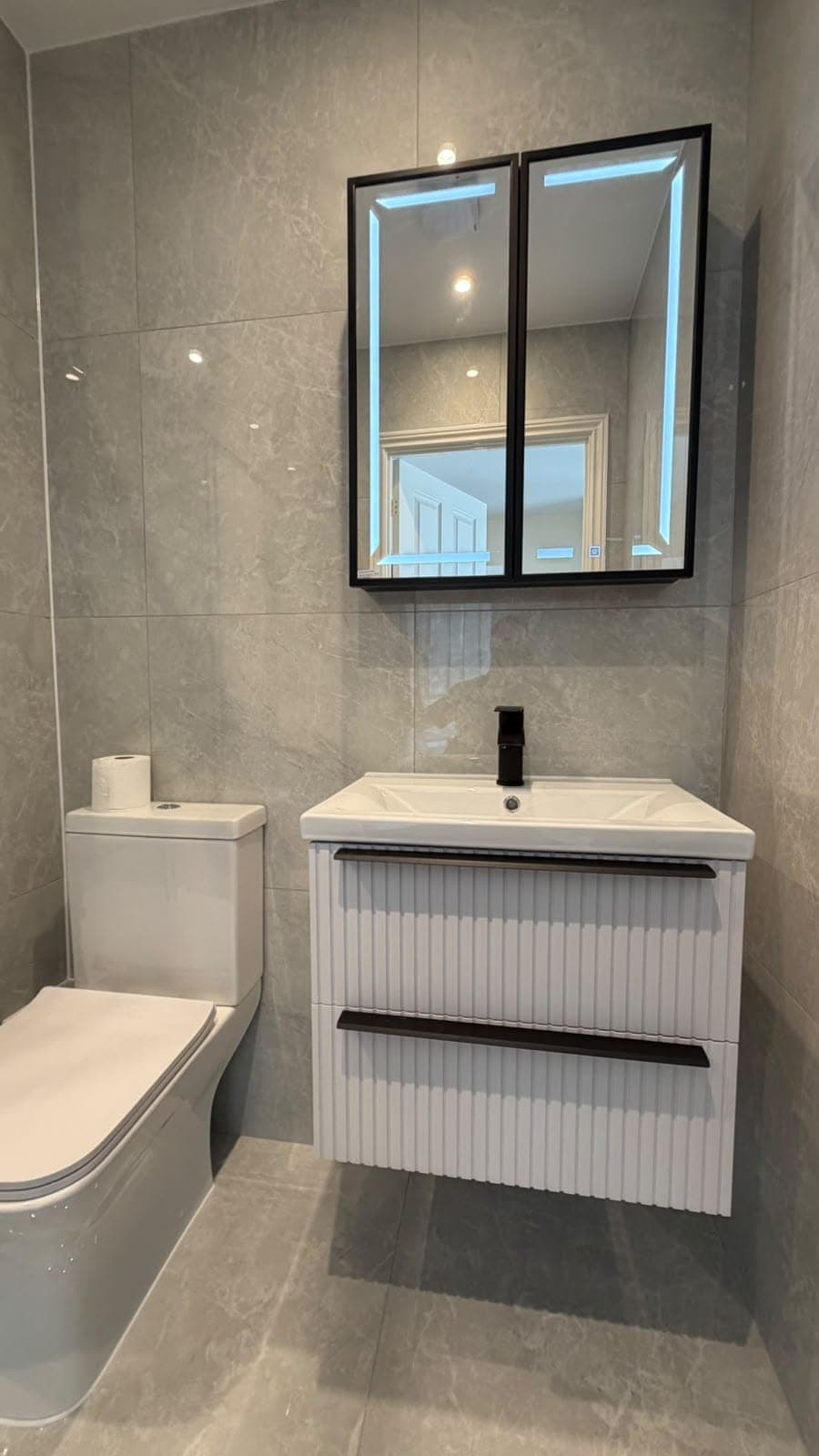 Bathroom with fluted white vanity unit, black mirror cabinet and grey wall tiles